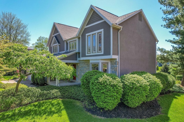 view of side of home with stucco siding, a lawn, and stone siding