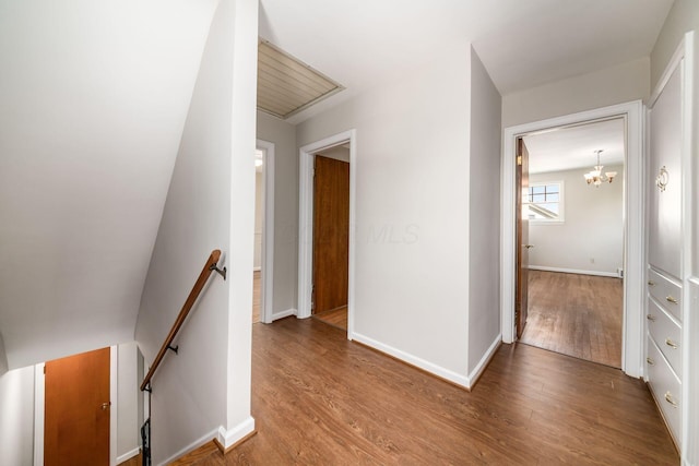 hall featuring baseboards, wood finished floors, a notable chandelier, and an upstairs landing