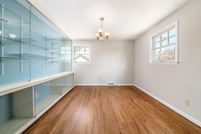 unfurnished dining area featuring baseboards, a chandelier, a healthy amount of sunlight, and wood finished floors