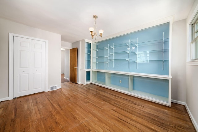 unfurnished dining area featuring baseboards, visible vents, an inviting chandelier, and wood finished floors