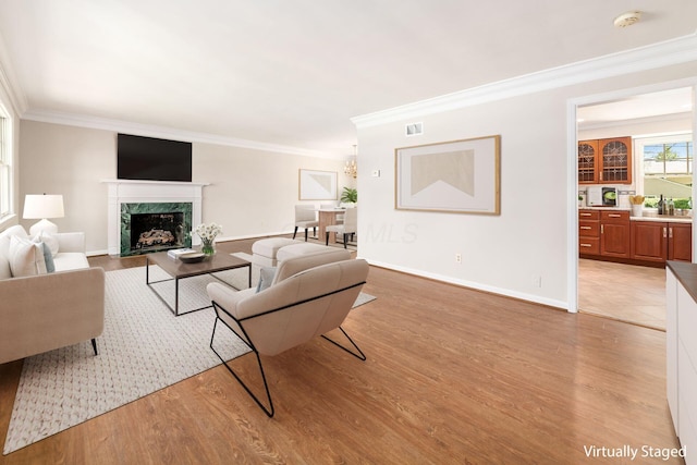 living area featuring visible vents, light wood finished floors, crown molding, and a premium fireplace