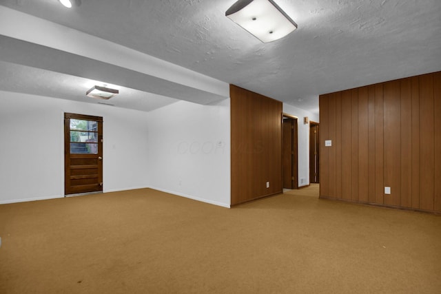 unfurnished room featuring a textured ceiling, baseboards, light colored carpet, and wood walls