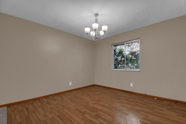 spare room featuring a notable chandelier, baseboards, visible vents, and light wood-style floors