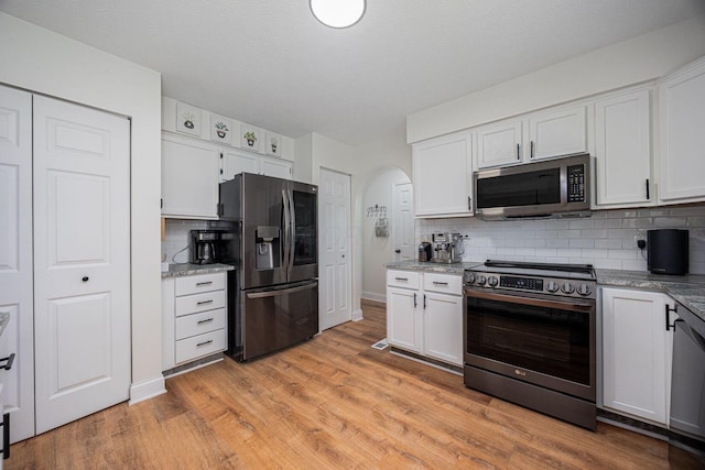 380 Oak Village Dr, Columbus, OH 43207 - kitchen with stainless steel appliances, decorative backsplash, white cabinets, arched walkways, and light wood-style floors