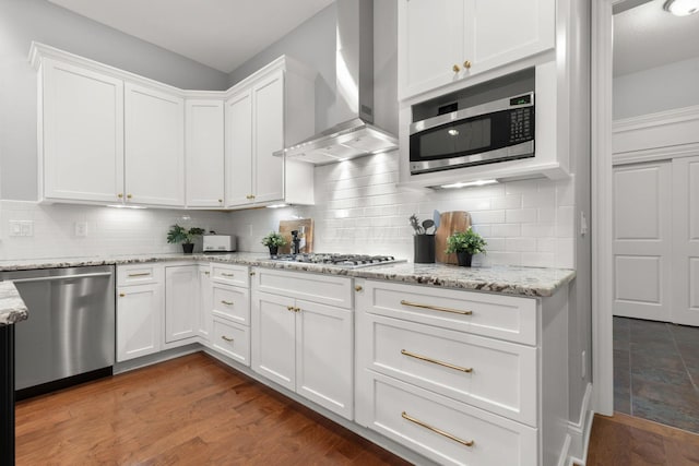 kitchen featuring wall chimney exhaust hood, tasteful backsplash, white cabinets, and stainless steel appliances