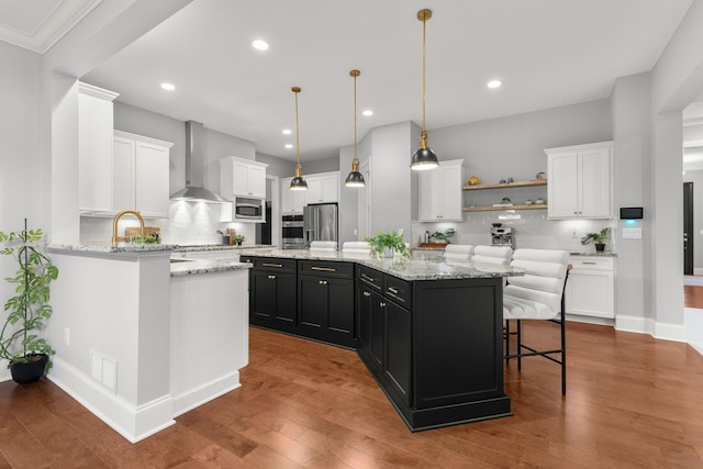 kitchen featuring a center island, wall chimney exhaust hood, white cabinetry, dark cabinetry, and stainless steel appliances