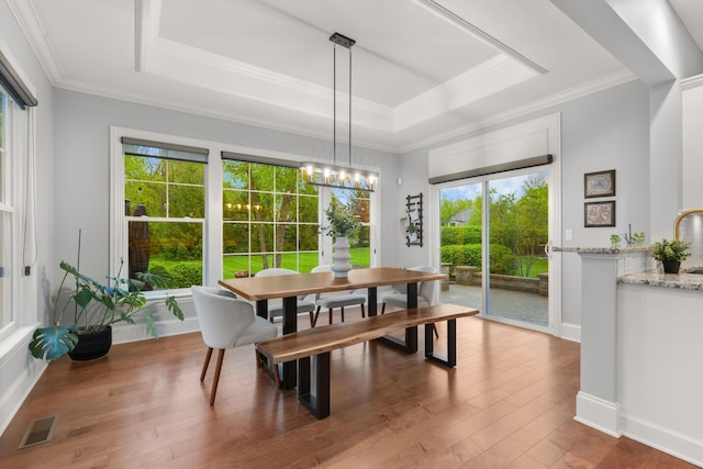 dining space with visible vents, hardwood / wood-style flooring, a raised ceiling, baseboards, and ornamental molding