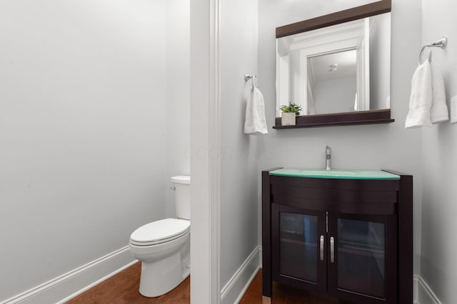 bathroom featuring toilet, baseboards, wood finished floors, and vanity