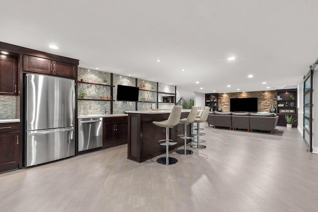 kitchen with dark brown cabinetry, appliances with stainless steel finishes, a center island, a breakfast bar, and light wood-style flooring