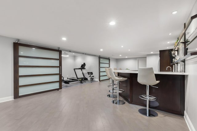 kitchen with a kitchen breakfast bar, dark brown cabinets, light countertops, light wood-style floors, and recessed lighting