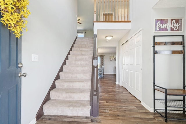 foyer with baseboards, stairway, wood finished floors, and a towering ceiling