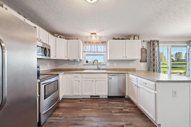 kitchen featuring a sink, stainless steel appliances, a peninsula, a textured ceiling, and white cabinets