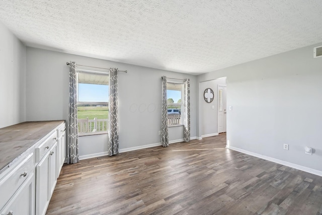 interior space with dark wood-style floors, visible vents, a textured ceiling, and baseboards
