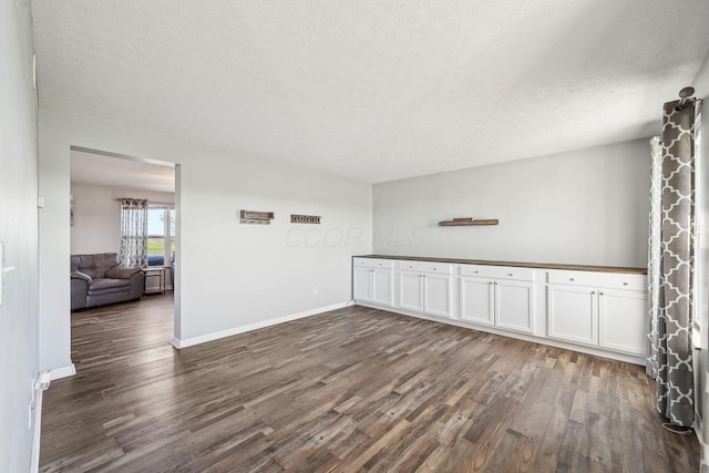 unfurnished room featuring a textured ceiling, baseboards, and dark wood-type flooring