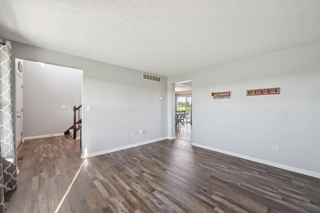 unfurnished living room featuring visible vents, baseboards, stairway, a textured ceiling, and dark wood-type flooring