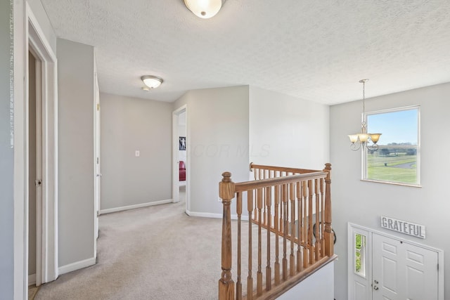 hallway featuring a chandelier, light carpet, an upstairs landing, baseboards, and a textured ceiling