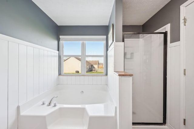 full bathroom with wainscoting, a stall shower, a textured ceiling, and a bath
