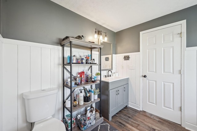 bathroom featuring wood finished floors, wainscoting, toilet, vanity, and a textured ceiling