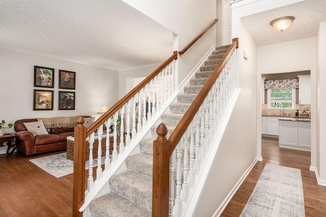 stairway with baseboards, wood finished floors, a textured ceiling, and ornamental molding