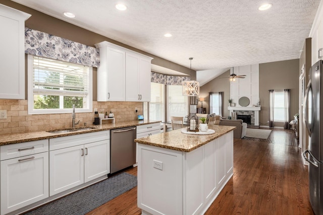 kitchen with a textured ceiling, white cabinets, a sink, stainless steel appliances, and a center island