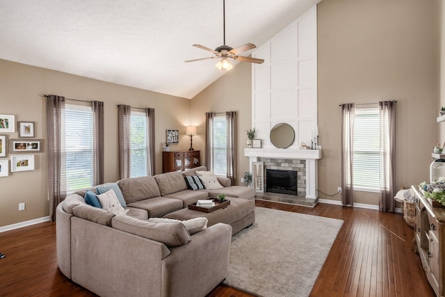 living area featuring a fireplace with raised hearth, baseboards, dark wood-type flooring, a ceiling fan, and high vaulted ceiling