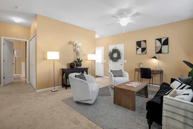 living area featuring a ceiling fan, baseboards, and light colored carpet
