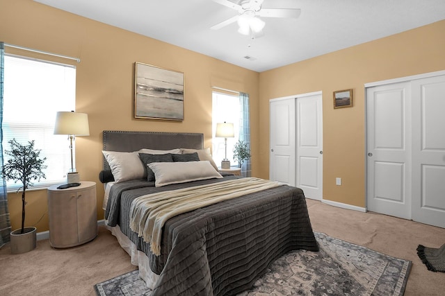 bedroom featuring two closets, baseboards, light colored carpet, and multiple windows