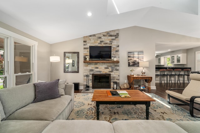 living room featuring a stone fireplace, baseboards, wood finished floors, and vaulted ceiling