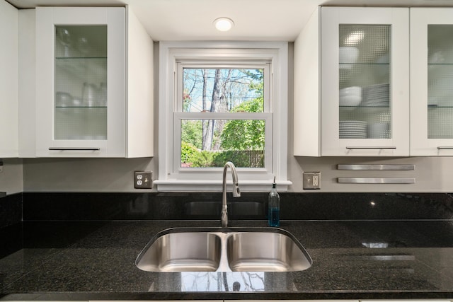 kitchen with a sink, dark stone countertops, white cabinets, and glass insert cabinets