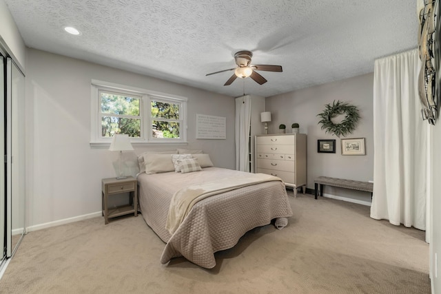bedroom with baseboards, a ceiling fan, a textured ceiling, and light colored carpet