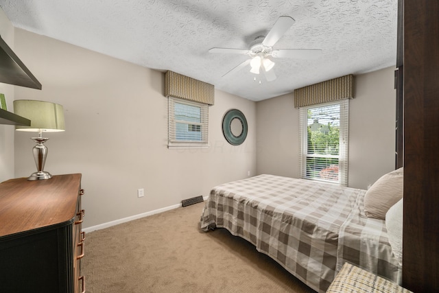 bedroom with baseboards, a ceiling fan, a textured ceiling, and light carpet