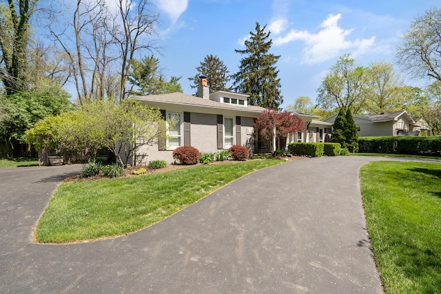 view of front facade featuring stucco siding, driveway, a chimney, and a front lawn