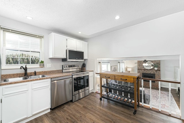 kitchen featuring a sink, dark wood-type flooring, a textured ceiling, white cabinets, and appliances with stainless steel finishes
