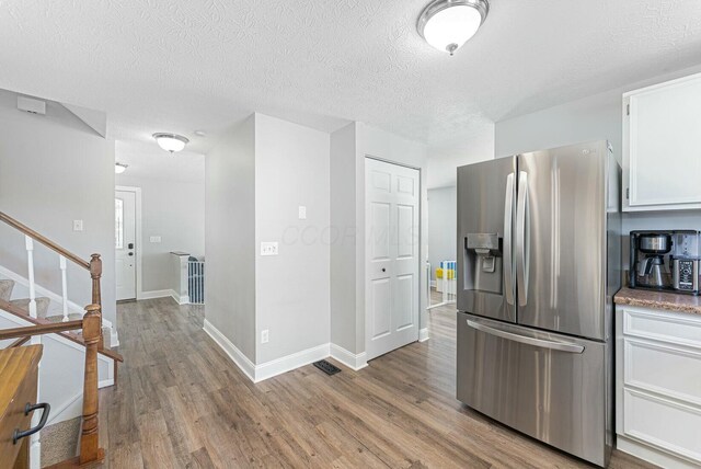 kitchen featuring a textured ceiling, white cabinetry, baseboards, light wood-type flooring, and stainless steel fridge with ice dispenser