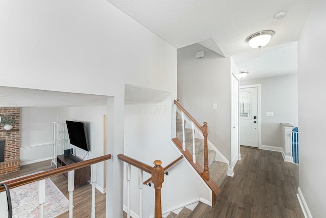 corridor featuring a textured ceiling, wood finished floors, baseboards, and stairs