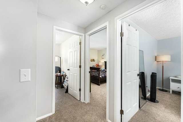 hall featuring light colored carpet, baseboards, and a textured ceiling