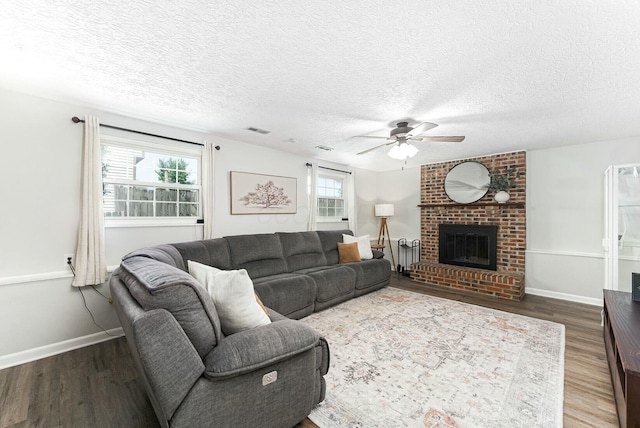 living area featuring a fireplace, a ceiling fan, visible vents, a textured ceiling, and wood finished floors
