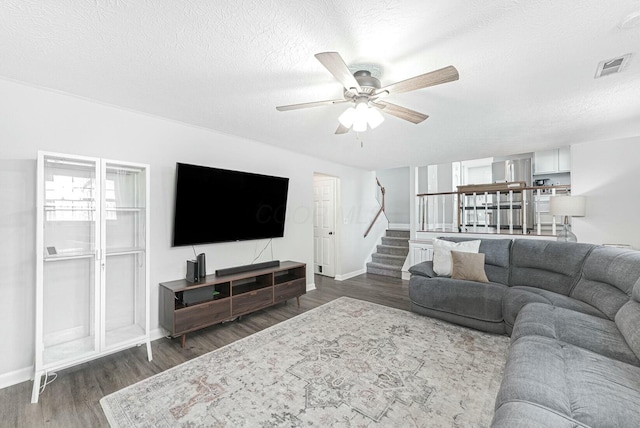 living area with visible vents, baseboards, dark wood-style flooring, a ceiling fan, and stairs