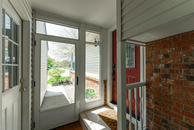 doorway to outside with tile patterned floors, brick wall, and plenty of natural light