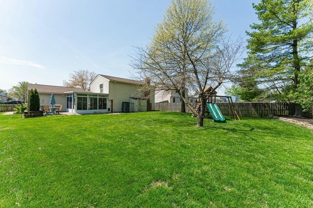 view of yard featuring a playground, a fenced backyard, central AC unit, and a sunroom