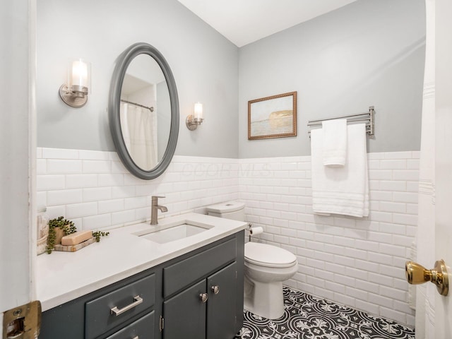 full bath with tile walls, vanity, tile patterned floors, toilet, and a wainscoted wall
