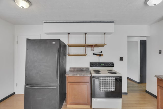kitchen with white electric range, freestanding refrigerator, a textured ceiling, and light wood-type flooring