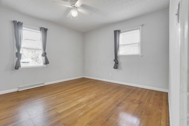 empty room featuring ceiling fan, a baseboard heating unit, a wealth of natural light, and hardwood / wood-style flooring