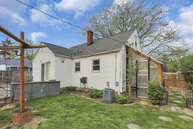 back of property featuring a greenhouse, a fenced backyard, a chimney, central air condition unit, and a yard