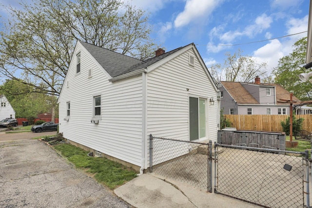 view of property exterior with a gate, roof with shingles, fence, and a chimney