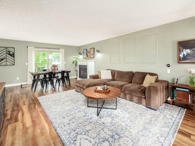 living area with baseboards, a textured ceiling, light wood finished floors, and a glass covered fireplace