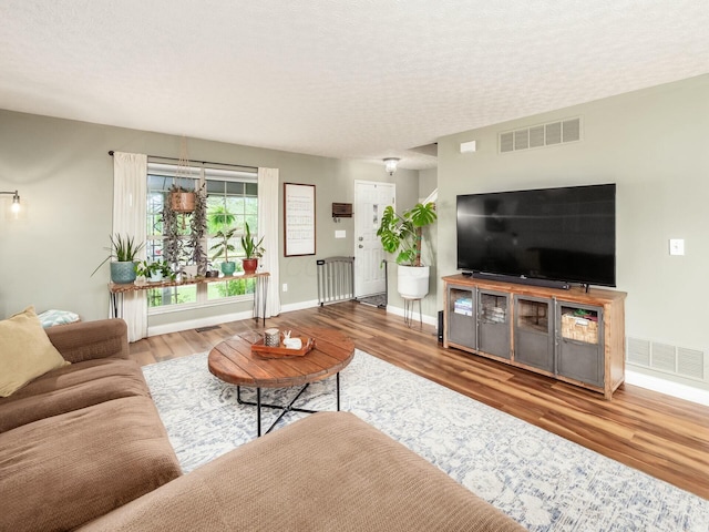 living room with a textured ceiling, visible vents, wood finished floors, and baseboards
