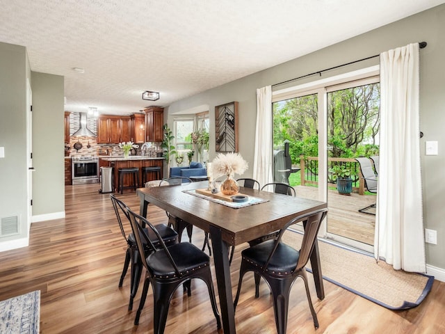 dining room featuring a textured ceiling, visible vents, baseboards, and light wood-style floors