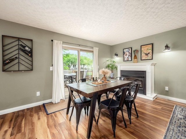 dining room featuring baseboards, a textured ceiling, light wood finished floors, and a glass covered fireplace