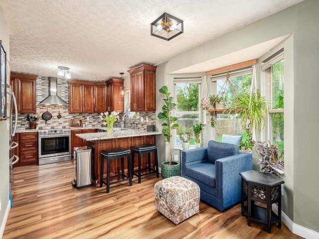kitchen featuring light wood-type flooring, wall chimney exhaust hood, backsplash, a peninsula, and stainless steel electric stove